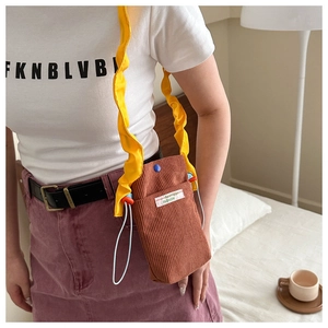 Brown corduroy crossbody phone bag featuring a vibrant yellow ruffled strap worn by model