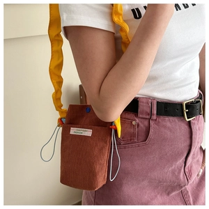 Detail of brown corduroy crossbody bag with yellow ruffled strap and blue drawstring