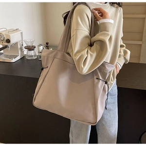 Large capacity tote bag with drawstring detail shown in a cafe setting worn by a model