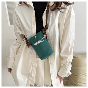 Detail of green corduroy crossbody bag with pink label and pleated shoulder strap