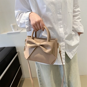 Light coffee leather crossbody bag with oversized bow detail held by a model