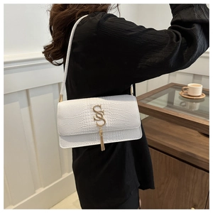 Close-up of white croc-embossed underarm bag with gold S-buckle and tassel on model