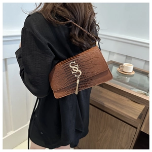Detail of brown crocodile pattern shoulder bag with a gold S-logo and metal tassel