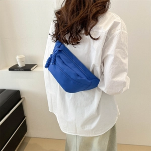 Blue canvas crossbody bag with woven zipper pull worn by model in minimalist studio