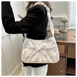 Detailed view of a white satin shoulder bag with pleated texture and decorative bow accent