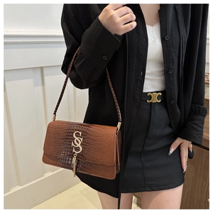 Detail of brown crocodile pattern shoulder bag with golden S logo and tassel fringe