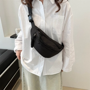 Minimalist black nylon crossbody sling bag with woven zipper pull worn by female model