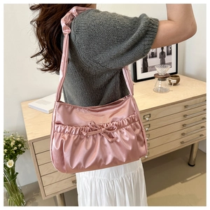 Close-up of pink satin pleated shoulder bag with decorative bow in a cozy indoor setting