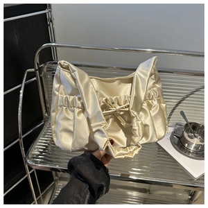 Detail of champagne gold satin handbag with elegant pleats and decorative bow accent