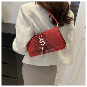 Detail of red crocodile textured shoulder bag with gold metal logo and tassel charm