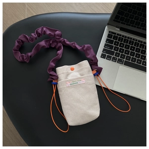Detail of corduroy phone bag with purple ruffled strap and orange drawstring accents