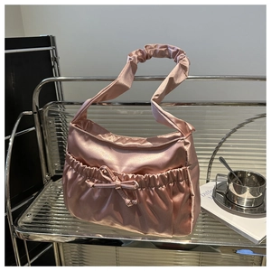 Detail of pink satin shoulder bag with pleated ribbon bow on a modern shelf