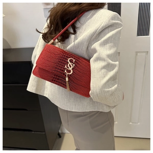 Detail of red faux crocodile skin underarm bag featuring gold hardware and metallic tassel