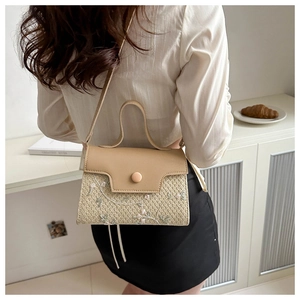 Detail of floral embroidery on a woven beige crossbody handbag with a leather flap