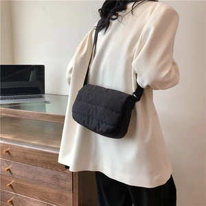 Sac à bandoulière matelassé noir minimaliste avec large sangle porté par un mannequin