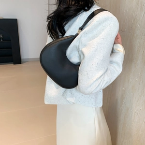 Minimalist black crescent shoulder bag with gold hardware worn on a white tweed jacket