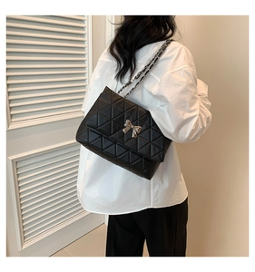 Détail du sac à bandoulière noir matelassé avec nœud argenté et bandoulière chaîne