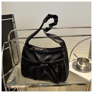 Detail of black satin shoulder bag featuring unique pleated strap and decorative bow pocket