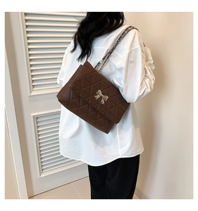 Détail du sac bandoulière matelassé marron avec boucle nœud porté par un mannequin