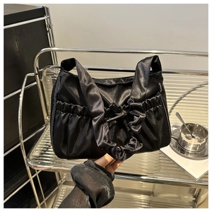 Detail of black pleated satin handbag with a decorative bow knot on a metal shelf
