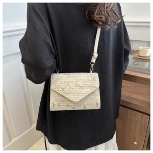 Detail of woven straw envelope bag featuring delicate floral embroidery and leather strap