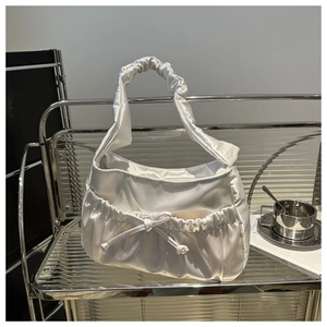 White satin handbag with ruched handle and bow detail on a minimalist glass shelf