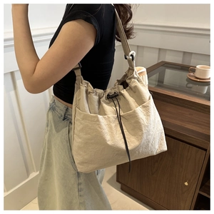 Dettaglio della borsa a secchiello in nylon crema con coulisse indossata da una modella