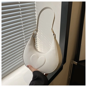 Detail of white crescent bag with embossed heart and gold metal ring hardware
