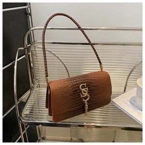 Detail of brown crocodile pattern shoulder bag with golden S logo and tassel hardware