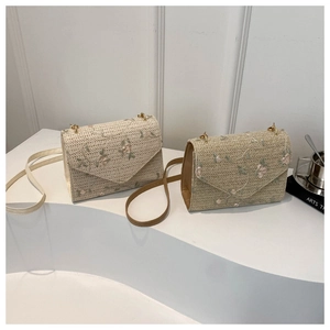 Detail of hand-woven straw crossbody bags featuring delicate pink floral embroidery and metal hardware
