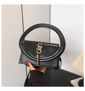 Detail einer schwarzen Lederhandtasche mit Rundgriff, goldenem S-Verschluss und Quaste