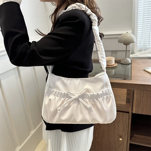 White satin shoulder bag with bow drawstring and pleated texture in chic interior setting