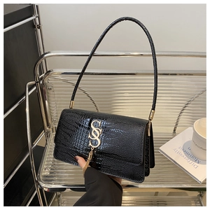 Close-up of black crocodile-embossed underarm bag with gold S logo and metal tassels