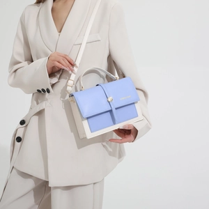 Sac bandoulière minimaliste bleu et crème avec boucle dorée porté par un mannequin