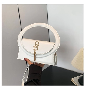 Detail der weißen Handtasche mit rundem Griff und goldenem S-Logo mit Metallquaste