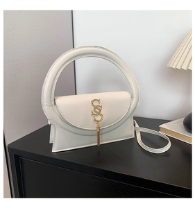 Detail der weißen Lederhandtasche mit rundem Griff und goldenem Quastenanhänger
