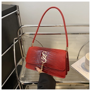 Detail of red crocodile texture handbag featuring a gold S-clasp and metallic tassel