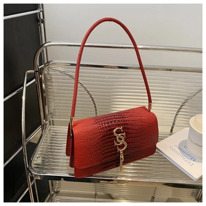 Detail of red crocodile texture handbag with gold S-buckle and tassel on a shelf