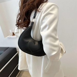 Minimalist black crescent shoulder bag with embossed heart detail worn by a model