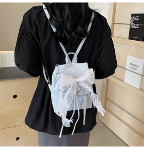 Close-up of light blue backpack with large white lace bow and drawstring closure detail
