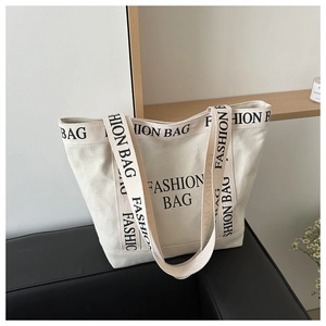 Detail view of beige canvas tote bag with black FASHION BAG print on leather sofa