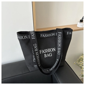 Close-up of large black canvas tote bag with bold white FASHION BAG letter prints