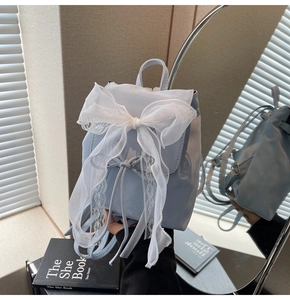 Close-up of light blue mini backpack with a large white lace bow and glossy finish