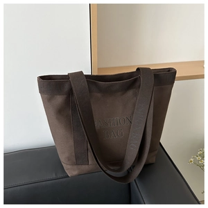 Close-up of dark brown canvas tote bag with fashion lettering on a leather sofa
