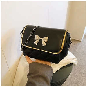 Close-up of black quilted crossbody bag with gold metal trim and silver bow clasp