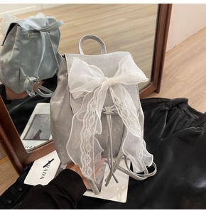 Detailed view of grey mini backpack featuring a large white lace bow and drawstring
