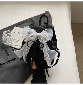 Close-up of black mini backpack featuring a large white lace bow and drawstring closure