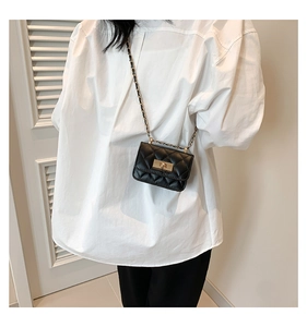 Dettaglio di una mini borsa a tracolla nera trapuntata con catena dorata indossata dal modello