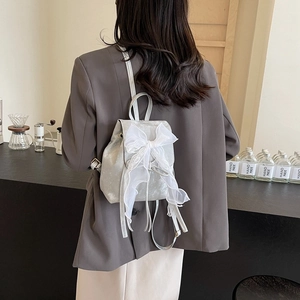 Silver mini backpack with white lace bow detail shown on a model in a cafe setting