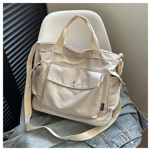 Detail of a beige canvas tote bag with fashion tag and wide strap on white chair